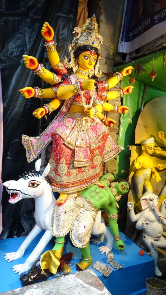 A small idol of yellow-skinned Durga standing on a green demon and riding a white horse is waiting for the  collection at Kumartuli district before Durga Puja