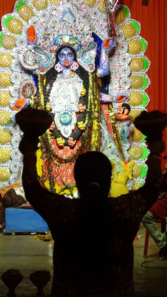 A woman dancing dhunuchi lifts claypots in front of the Kali idol during Kali puja in Kolkata