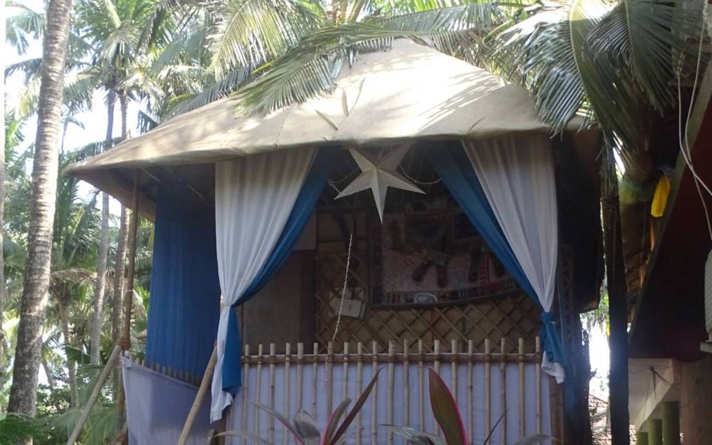 A basic bamboo hut on stilts with a veranda and decoration from colourful textiles stands in a coconut grove on Agonda Beach 