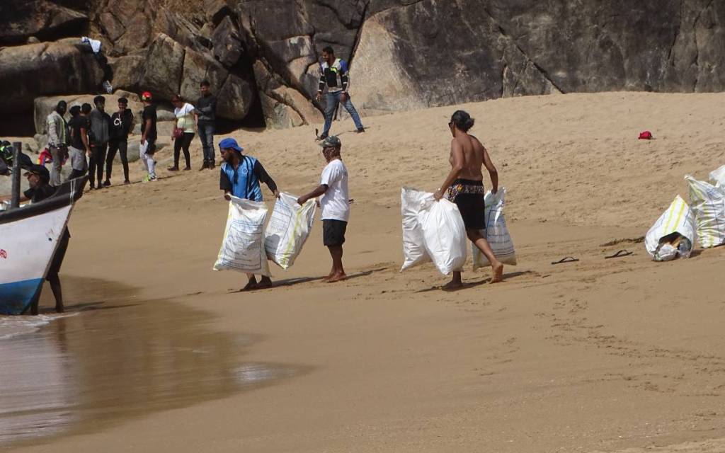 Local tourists watch by as a group of Indian volunteers pack sacks of garbage onto a boat on Butterfly Beach in Goa