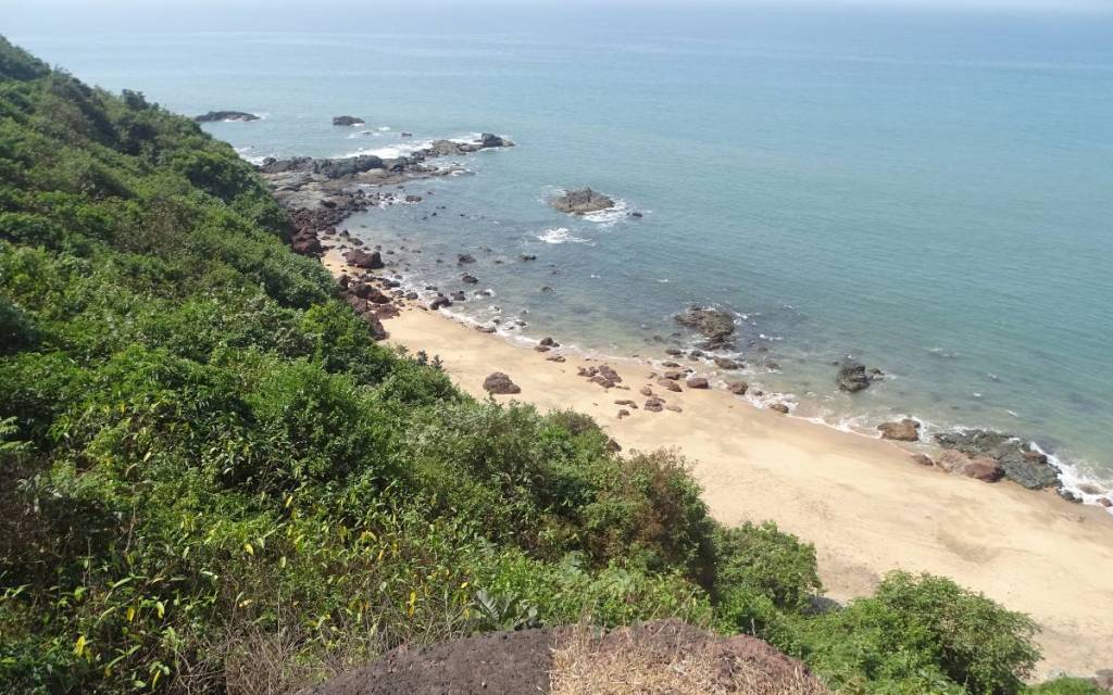 A view from the top of a cliff at a virgin sand beach peppered with boulders 